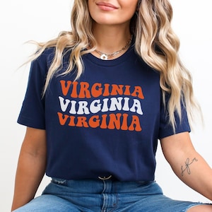 May include: A navy blue t-shirt with the word "VIRGINIA" repeated three times in a retro font. The text is in orange and white.