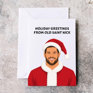 May include: A white greeting card featuring a cartoon illustration of a smiling person with a beard wearing a red Santa hat and a red coat with white fur trim. The text HOLIDAY GREETINGS FROM OLD SAINT NICK is printed in black at the top.