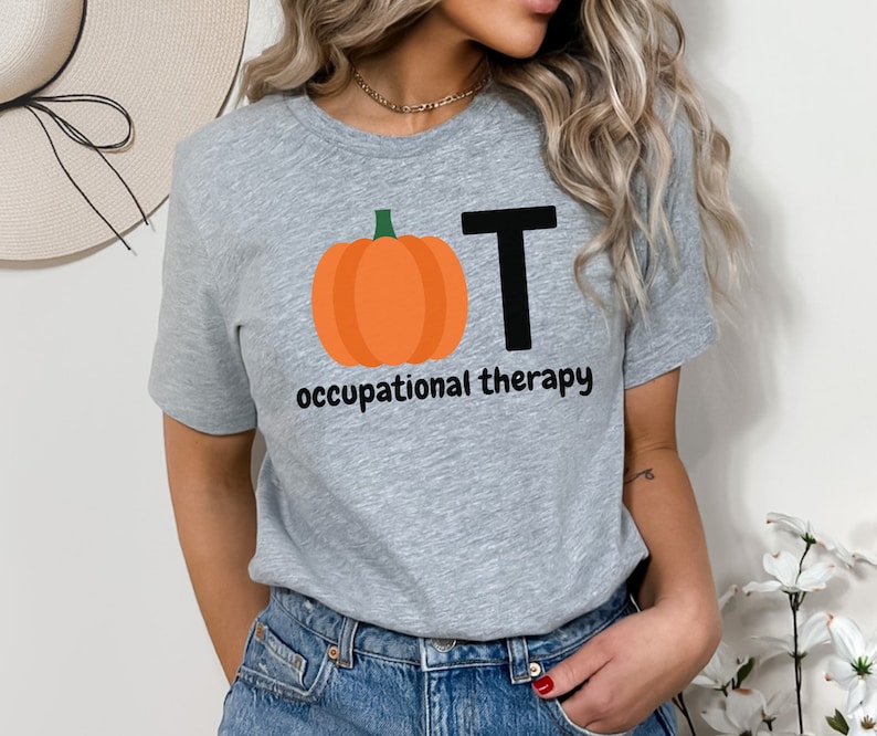 May include: A heather gray t-shirt featuring a pumpkin graphic with the letters "OT" and the words "occupational therapy" in black. The pumpkin is orange with a green stem. The shirt is made of a soft material.