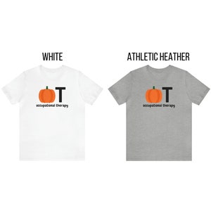 May include: Two t-shirts, one white and one athletic heather, each displaying a pumpkin graphic with the letters "OT" and the words "occupational therapy" in black. The pumpkin is orange with a green stem.
