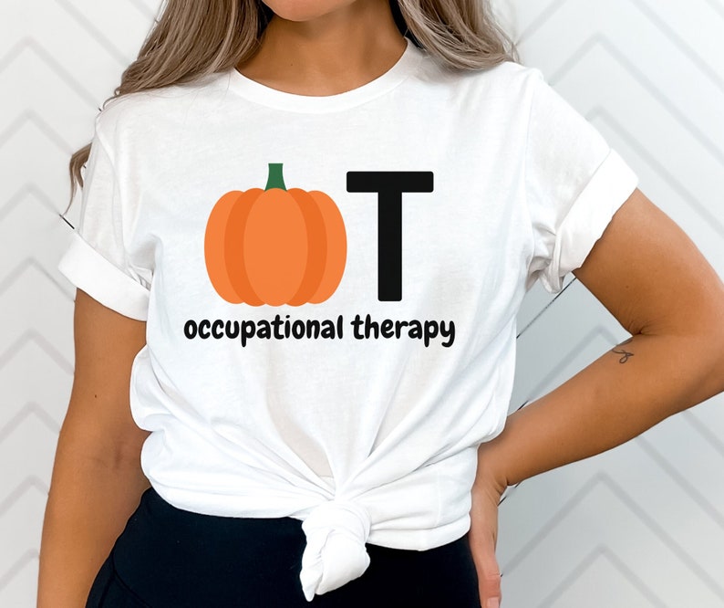 May include: White t-shirt featuring a pumpkin graphic and the letters "OT" in black, with the words "occupational therapy" below. The pumpkin is orange with a green stem. The shirt is made of a soft material.