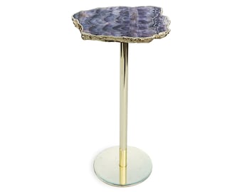 May include: A purple amethyst table with a gold metal base. The table top is a natural slice of amethyst with a unique shape and pattern.