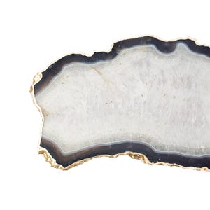 May include: A polished agate slice coaster featuring a translucent white crystalline center surrounded by concentric bands of dark gray and black, finished with a metallic gold-toned electroplated edge along the irregular, organic outer perimeter.