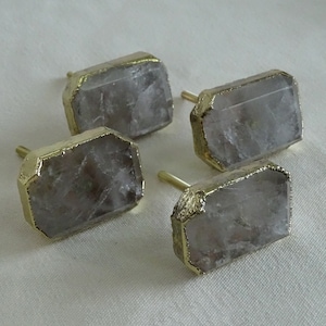 Puede incluir: Cuatro pomos de armario de cristal transparente con ribete de metal dorado. Los pomos son de forma rectangular y tienen un diseño facetado.