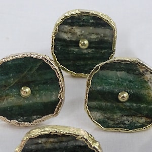 May include: Four green and gold agate drawer pulls with a round knob in the centre. The agate is a dark green with white and grey streaks.