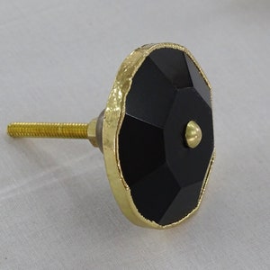 May include: Black and gold cabinet knob with a faceted design. The knob has a gold metal rim and a black, faceted centre.
