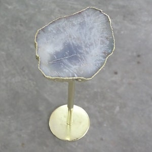 May include: A white agate slice table top with a gold rim sits on a gold metal stand with a round base.