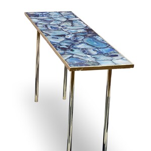 May include: A long, rectangular table with a blue agate top and a gold trim. The table has two chrome legs.