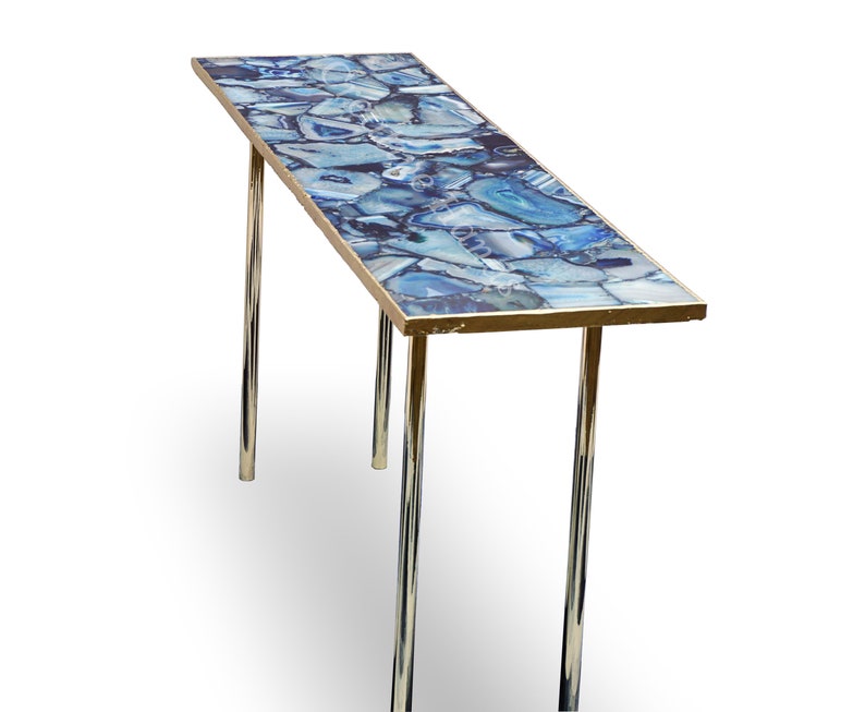 May include: A long, rectangular table with a blue agate top and a gold trim. The table has two chrome legs.