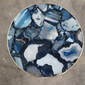 May include: A round table top made of blue and white agate stone. The table top is surrounded by a gold metal rim.
