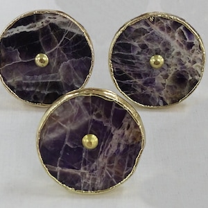 May include: Three round purple and gold cabinet knobs with a gold rim and a gold knob in the center.