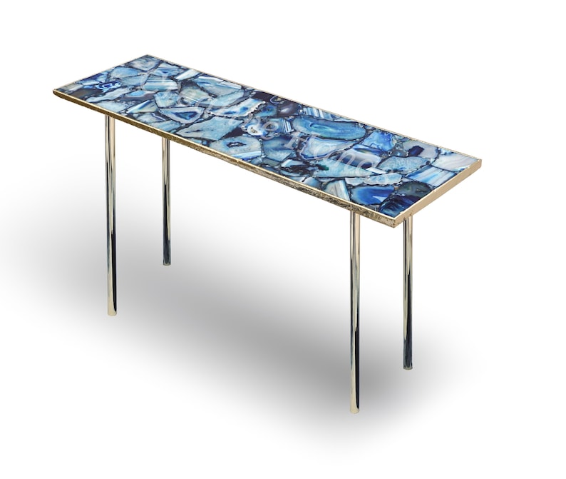 May include: A long, rectangular console table with a blue agate stone top and a polished gold metal frame. The table has two chrome legs.