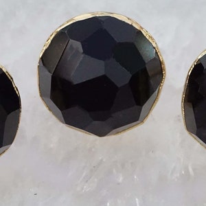 May include: Three black gemstone earrings with gold settings. The gemstones are faceted and have a round shape.