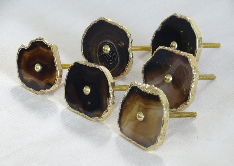 以下が含まれることがあります： 金色のトリムが付いたアゲート製の引き出しノブ6個。各ノブには、金色のネジが付いた、ユニークな茶色と白のアゲートのスライスが特徴です。