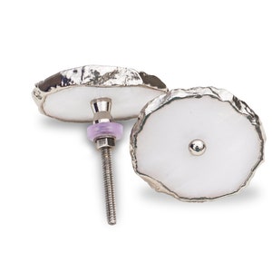 Puede incluir: Dos tiradores de cajón de ágata blanca con ribete de metal plateado. Los tiradores tienen un borde áspero y natural y una parte posterior atornillable.