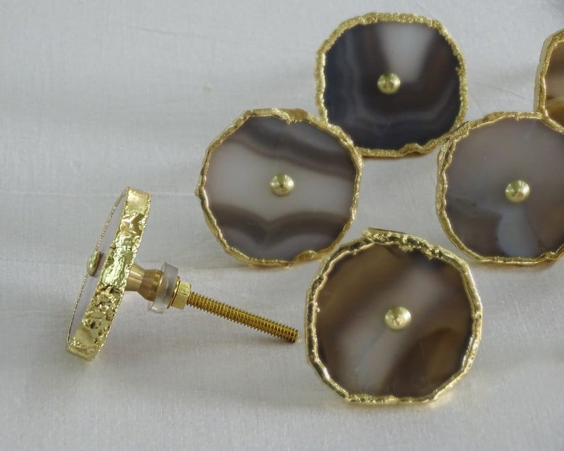 May include: Set of six agate drawer pulls with gold trim. Each pull features a unique pattern of brown and white agate.