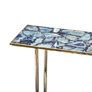 May include: A modern console table with a blue agate top and gold trim. The table has a rectangular top and two chrome legs.