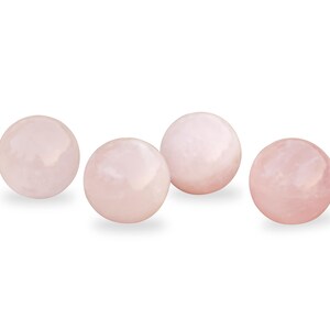 Pu&ograve; includere: Quattro sfere lisce di quarzo rosa, ciascuna delle dimensioni di una palla da golf, sono disposte in fila su uno sfondo bianco.