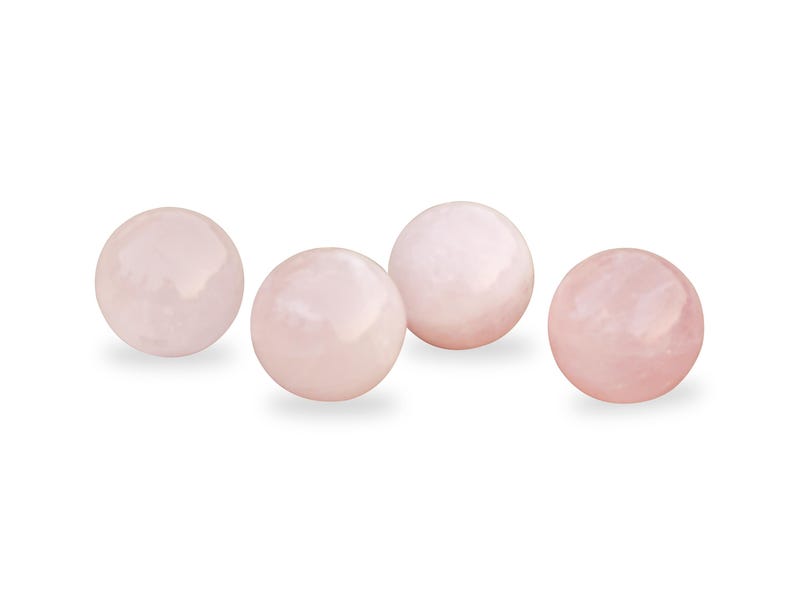 Pu&ograve; includere: Quattro sfere lisce di quarzo rosa, ciascuna delle dimensioni di una palla da golf, sono disposte in fila su uno sfondo bianco.