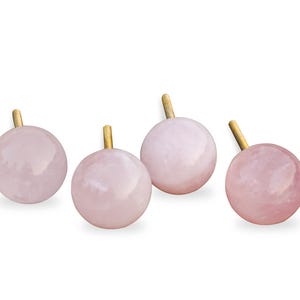 Pu&ograve; includere: Quattro pomelli in quarzo rosa con steli in metallo dorato. I pomelli sono rotondi e hanno una finitura liscia e lucida.