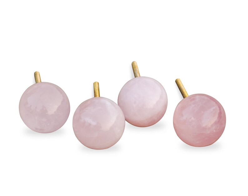 Pu&ograve; includere: Quattro pomelli in quarzo rosa con steli in metallo dorato. I pomelli sono rotondi e hanno una finitura liscia e lucida.