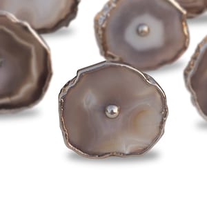 Puede incluir: Un juego de seis tiradores de cajones de ágata con ribete de metal plateado. Cada tirador presenta un patrón de ágata natural único en tonos grises y blancos.