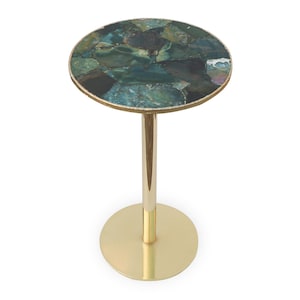 Puede incluir: Una pequeña mesa auxiliar redonda con base y tallo de metal dorado. La tapa es un mosaico de piedras verdes y verde azulado, con un borde dorado. La mesa mide aproximadamente 51 cm de altura.