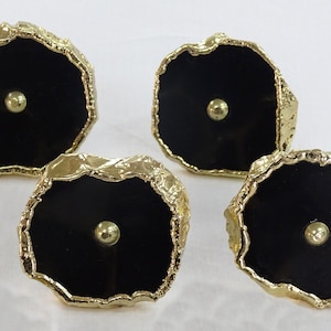 May include: Four black and gold agate drawer pulls with a round knob in the centre. The pulls have a rough, natural edge.