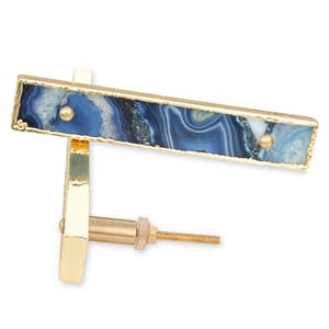 May include: A rectangular drawer pull featuring a blue and white agate stone inlay set within a gold-toned metal frame. The hardware includes a central gold-toned post with a threaded screw for mounting, and two small gold-toned rivets on the stone face.