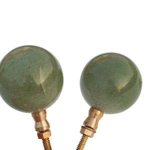 May include: Two green ceramic finials with brass bases. The finials are round and have a smooth, slightly textured surface.