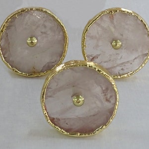 Pode incluir: Três botões redondos de quartzo rosa com acabamento em metal dourado. Cada botão tem uma pequena bola de metal dourado no centro.