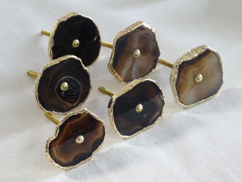 以下が含まれることがあります： 金色の縁取りが施された茶色の瑪瑙製の引き出しノブが6つ。各ノブの中央には小さな金色のノブがあります。