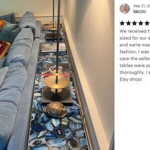 May include: Two custom-sized agate tables with a gold metal stand and a blue velvet sofa with pillows. The tables are made of blue and white agate slices.