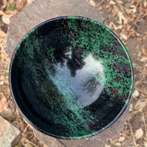 May include: A green and black bowl made of polished stone. The bowl has a swirling pattern of green and black with hints of pink.