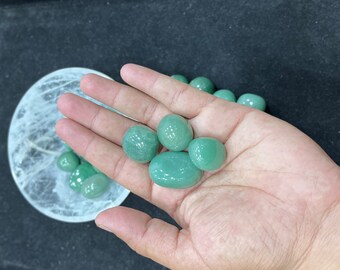 May include: A hand holding a collection of smooth, green jade stones. The stones are various sizes and shapes, and have a polished, glossy finish.
