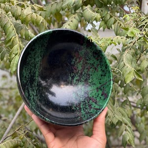 May include: A black and green bowl made of polished stone. The bowl has a speckled pattern of green and black.