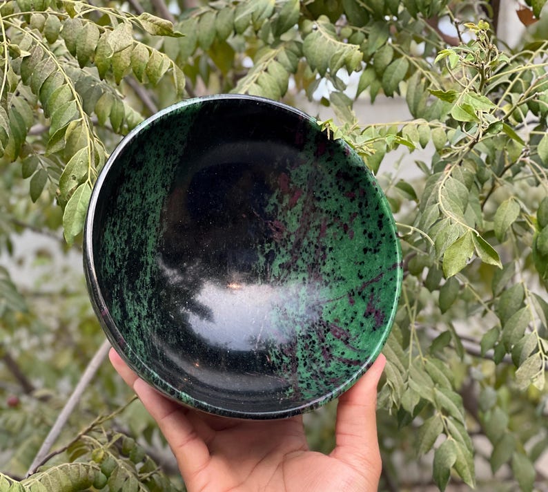 May include: A black and green bowl made of polished stone. The bowl has a speckled pattern of green and black.
