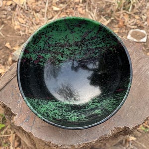 May include: A green and black bowl with a speckled pattern. The bowl is made of polished stone and has a smooth, glossy finish.
