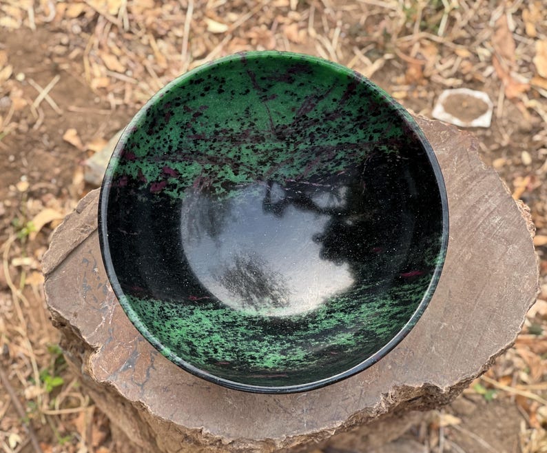 May include: A green and black bowl with a speckled pattern. The bowl is made of polished stone and has a smooth, glossy finish.