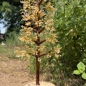 May include: A crystal tree made of clear and amber-colored stones, with a brown wooden base. The tree is standing on a wooden stump.