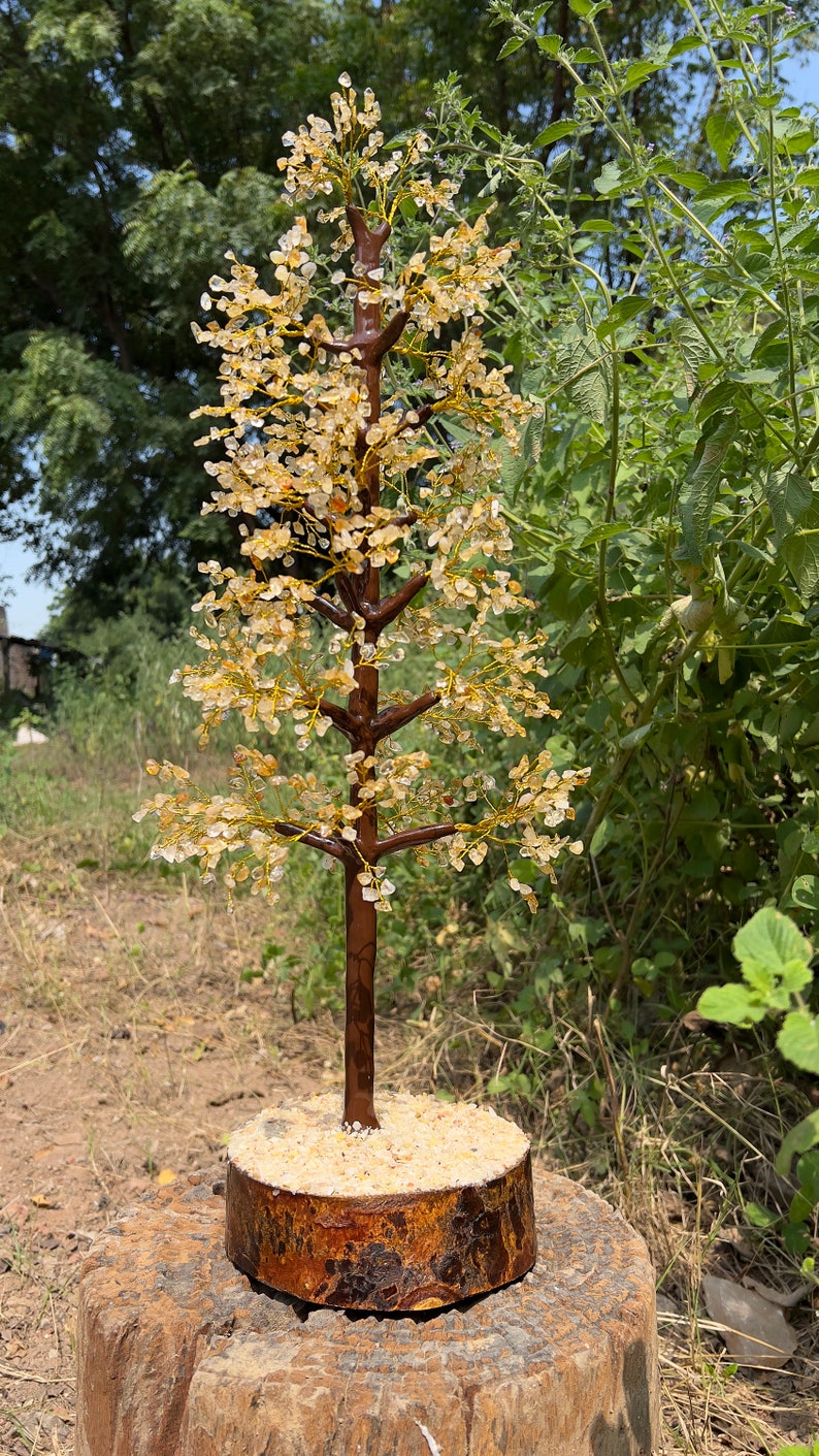 May include: A crystal tree made of clear and amber-colored stones, with a brown wooden base. The tree is standing on a wooden stump.