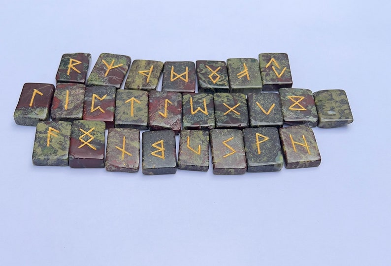 以下が含まれることがあります： 金色の文字が書かれた、緑色、茶色、黒色の石のルーン24個のセット。各ルーンは、ユニークなシンボルが刻まれた小さな長方形の石です。