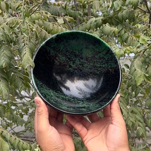 May include: A green and black bowl made of polished stone. The bowl has a smooth, rounded surface and a deep, wide interior.