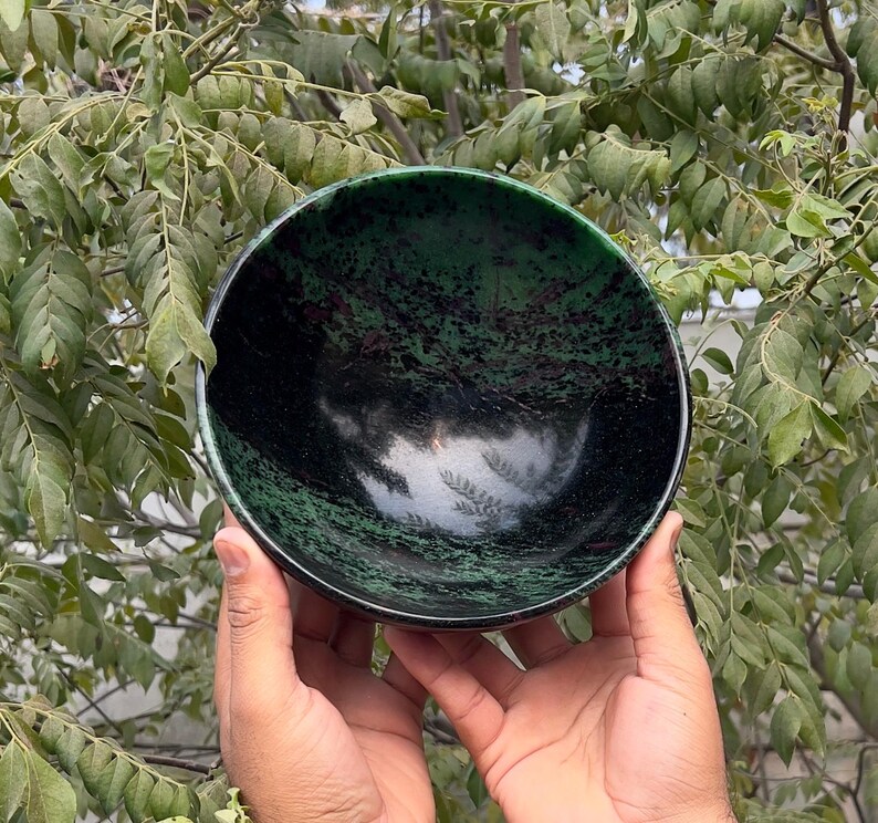 May include: A green and black bowl made of polished stone. The bowl has a smooth, rounded surface and a deep, wide interior.