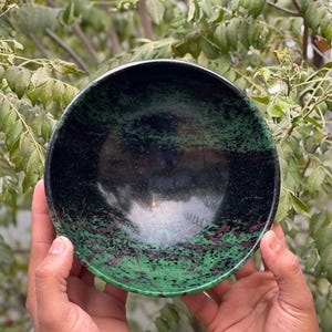 May include: A green and black bowl made of polished stone. The bowl has a speckled pattern with green, black, and pink hues.
