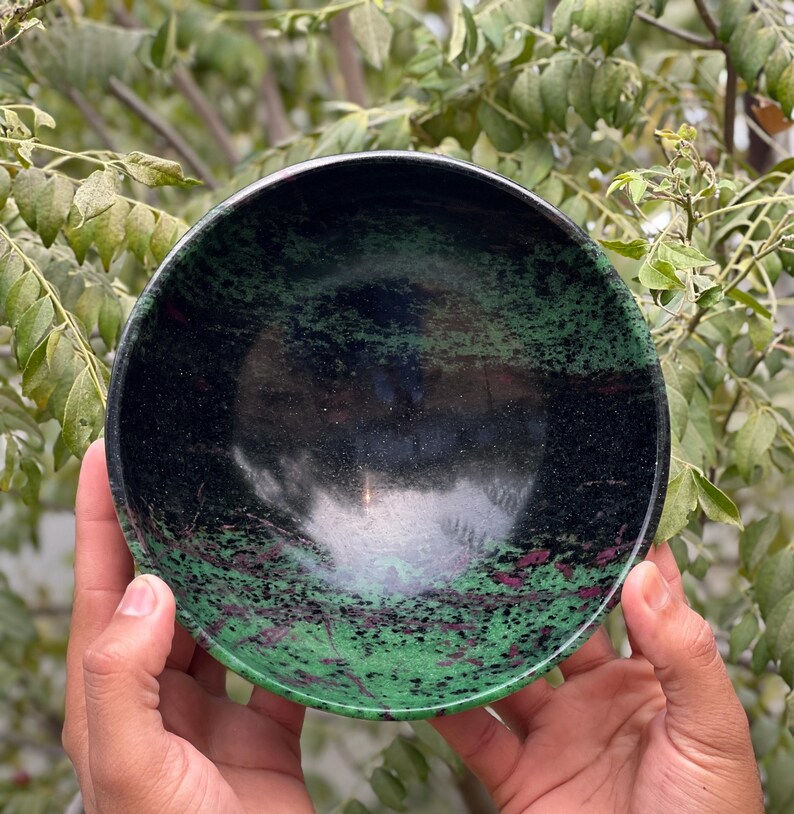 May include: A green and black bowl made of polished stone. The bowl has a speckled pattern with green, black, and pink hues.