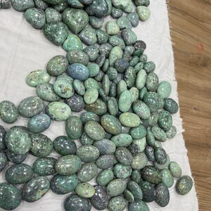 Może przedstawiać: Duża sterta zielonych i r&oacute;żowych kamieni szlifowanych. Kamienie są gładkie i owalne.