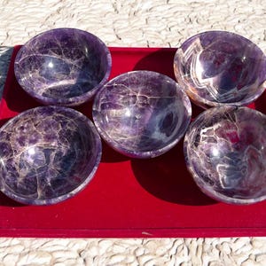 Könnte beinhalten: Fünf Amethyst-Schalen, jede mit einem einzigartigen, wirbelnden Muster, werden auf einem roten Samttablett präsentiert. Die Schalen sind aus natürlichem Amethystkristall gefertigt und haben eine tiefe violette Farbe.