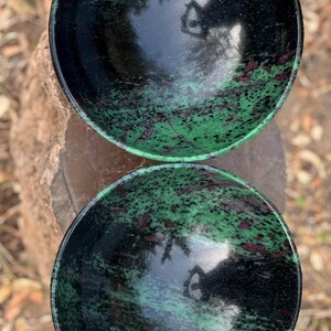 May include: Two black bowls with green and pink marbling. The bowls are made of polished stone and have a reflective surface.