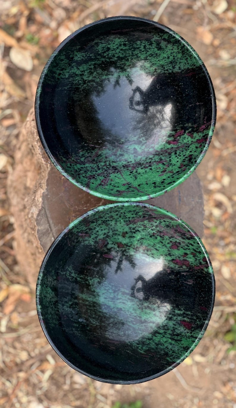 May include: Two black bowls with green and pink marbling. The bowls are made of polished stone and have a reflective surface.